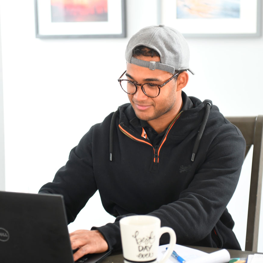 Man in backwards cap sitting at a desk working on laptop