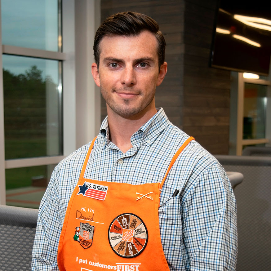 Man in decorated Home Depot apron smiles at camera in Store Support Center