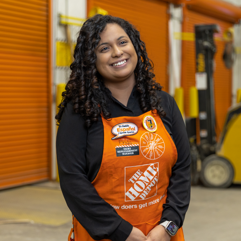 A young Latina women in an orange apron smiles while standing in a storage facility.
