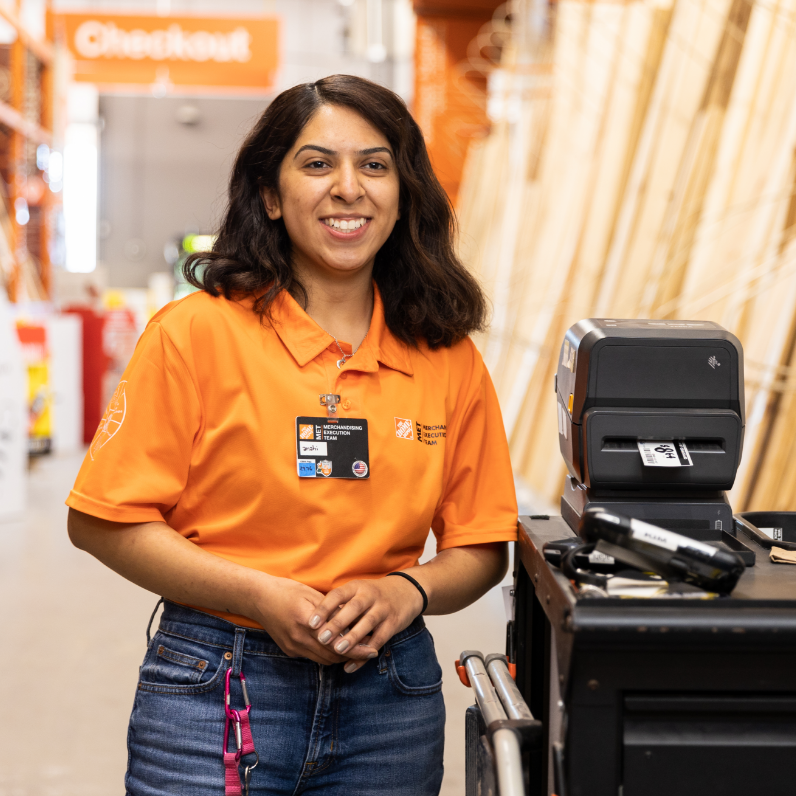 Young Latina woman in an orange polo shirt smiles as she leans against merchandising equipment.
