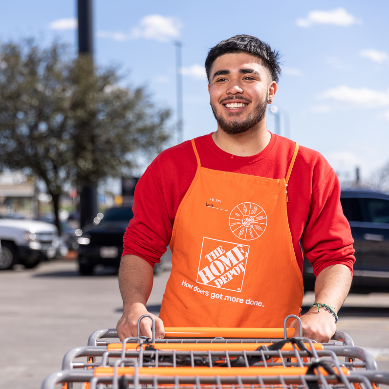 Young Latino man in red shirt and orange apron smiles as he collects shopping carts.